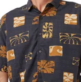 Camisa de manga corta negra con diseño estampado de bloques con motivos tropicales y abstractos en tonos tostados y beige, de corte clásico con cuello camisero y cierre frontal de botones.