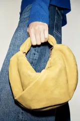Bolso de mano de piel color verde mostaza, con cuerpo fruncido, asa de mano con detalle retorcido, cadena metálica opcional para función bandolera y cierre mediante cremallera.