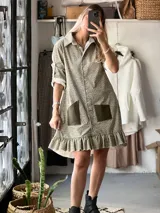 Vestido camisero de corte recto y largo por encima de la rodilla, confeccionado en pana elastizada con estampado floral pequeño. Presenta cuello camisero, cierre frontal con botones, mangas tres cuartos con puños vueltos, bolsillos frontales de cuero en contraste y ruedo con volado.