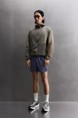 Chaqueta cortavientos de tejido técnico con estructura ripstop, cuello subido con capucha, cierre frontal de cremallera, bolsillos laterales ocultos y zonas perforadas para mayor transpirabilidad.