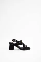 Sandalia de taco cuadrado medio, confeccionada en cuero vacuno negro. Presenta tiras cruzadas sobre el empeine decoradas con tachas metálicas doradas y cierre con hebilla ajustable en el tobillo.