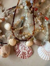 Collar largo de cuentas de piedras semipreciosas en tonos tierra, con dijes de conchas marinas.