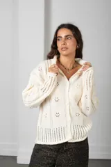 Cárdigan de punto color beige con textura calada de motivos florales, cuello alto, cierre frontal con botones y mangas largas con terminaciones acanaladas.