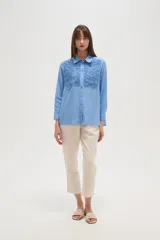 Camisa de manga larga color celeste, con cuello camisero y cierre frontal de botones. Presenta un diseño distintivo con paneles de encaje tipo crochet en la parte superior delantera.