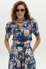 Camisa de lino azul con estampado floral en tonos rosados y beige, cuello mao con escote en V y mangas cortas abullonadas.