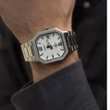 Reloj analógico Casio con caja octagonal de acero inoxidable y malla de eslabones plateada. Presenta una esfera blanca con índices aplicados, números 12 y 6, y ventana de calendario a las tres.