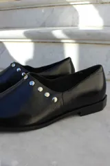 Zapato de cuero vacuno color bordó, con diseño de punta cuadrada y detalle de tachas metálicas planas en el borde superior. Presenta un taco geométrico bajo y costura central en el empeine.