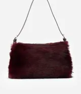 Cartera mediana de pelo sintético color bordó, con asa única de cuero sintético brillante, cierre superior por cremallera y detalles de argollas metálicas en los laterales.