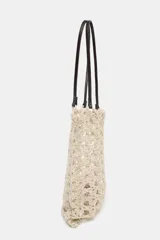Bolso tipo shopper de tamaño pequeño, tejido en crochet color beige claro con patrón calado. Incluye asas de hombro de cuero sintético marrón oscuro y una bolsa interior con cierre de cremallera.