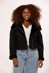 Campera corta tipo gamulán en color negro, con interior y detalles en puños y cuello de corderito sintético al tono. Presenta cierre frontal metálico y un botón decorativo en el ruedo.