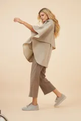 Capa amplia con capucha, confeccionada en lana fina sin teñir. Presenta cierre frontal, bolsillos delanteros y botones laterales que permiten ajustar la forma de las mangas.