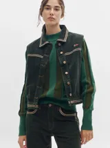 Chaleco de pana color verde oscuro, con cierre frontal de botones metálicos, cuello camisero y detalles de costuras en contraste. Presenta un pequeño bordado distintivo en el pecho.