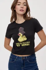 Remera blanca de manga corta, con estampa frontal de un pato de hule con turbante y labios pintados, acompañada de la frase "In all else fails, denial".