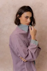 Camisa lila de calce relajado y manga larga, con cuello clásico, puños y bolsillo delantero en denim contrastante. Cierre frontal con broches metálicos.