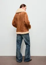 Chaqueta de efecto ante color marrón con forro y cuello de borreguito en tono crema. Presenta cierre frontal con cremallera, diseño recto y dos bolsillos laterales.