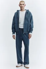 Campera con capucha de corte oversized, confeccionada en tejido de mezcla de algodón con interior suave. Presenta cierre frontal, hombros caídos, cordón ajustable en la capucha y bolsillos tipo canguro. Puños y bajo acanalados.
