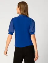 Blusa de color blanco con escote en V y detalle de lazo frontal. Presenta mangas cortas de gasa con terminación en puño.