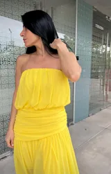 Vestido largo amarillo de estilo strapless, con cuerpo drapeado y falda fluida con tajo lateral.