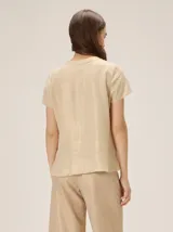 Camisa de manga corta color beige con estampado a cuadros, cuello en V y detalles de galones decorativos estilo oriental en la parte frontal.