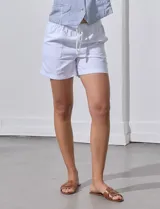 Short color crema con finas rayas verticales grises, pretina elastizada con cordón de ajuste, bolsillos delanteros y traseros.