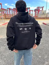 Canguro negro con capucha, de corte holgado y manga larga. Presenta un estampado gráfico en la espalda con el texto 'Community of talented people' y 'SOUTH CAPITAL' junto a iconos minimalistas.