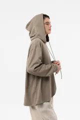 Buzo de punto oversize en color beige, con capucha, cordones largos ajustables y mangas largas amplias con puños elásticos. Presenta diseño asimétrico, más largo en la parte posterior.