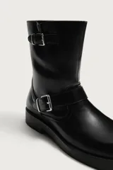 Bota de media caña color negro con horma cuadrada, suela con ligero tacón y ajuste mediante dos tiras con hebilla metálica, una en el empeine y otra en la parte superior de la caña.