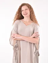 Vestido de tela fluida color marrón medio, con escote en V y mangas cortas tipo kimono. El ruedo es asimétrico con aberturas laterales.