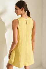 Vestido corto de lino italiano, sin mangas y con cuello redondo a la base. Presenta detalles desflecados en el cuello y costura central vertical.