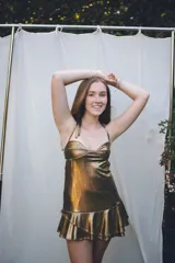 Vestido corto de tela satinada color plata, con diseño tipo corset en el top, breteles finos y falda con volados superpuestos.