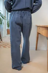Pantalón de denim blanco de corte amplio, con cierre de botón y cremallera, y detalles de tachas en los laterales y bolsillos.