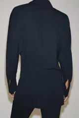 Blazer de corte fluido confeccionada en mezcla de viscosa, con cuello solapa, manga larga con puños abotonados y cierre frontal cruzado con botón único.