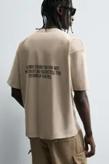 Camiseta de corte relaxed fit, color beige claro con efecto lavado, cuello redondo y manga corta. Estampado frontal en negro con texto "SUNSET ERA" y un caballo galopando.