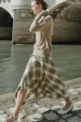 Falda midi de tiro alto con diseño asimétrico y estampado de cuadros en tonos beige, marrón y negro. Presenta una abertura frontal con acabados desflecados y cierre lateral con cremallera oculta.