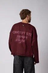 Buzo de cuello redondo confeccionado en tejido rústico con bordes al corte y costuras expuestas. Presenta un diseño boxy con estampado frontal y es reversible, permitiendo su uso por ambos lados.