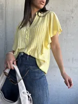 Camisa amarilla de mangas cortas con volados, cuello mao y botones frontales.