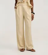 Pantalón de vestir de mujer, tiro alto, corte wide leg, color beige claro. Presenta pliegues frontales y frisos marcados.