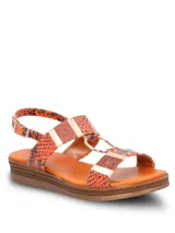 Sandalia de plataforma baja con tiras estampadas en animal print de serpiente en tonos naranja y negro. Presenta detalles de apliques metálicos dorados y texturas brillantes, con cierre mediante hebilla ajustable en el tobillo y plantilla de color suela.