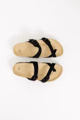 Sandalias planas de color negro con tiras ajustables mediante hebillas metálicas y diseño con separación para el dedo. Cuenta con plantilla acolchada y suela de corcho.