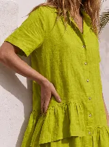 Vestido camisero corto de lino color blanco, con mangas cortas, cierre frontal de botones, cuello camisero y volados asimétricos en el ruedo.