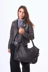 Cartera tipo bolso de hombro color negro, confeccionada en material simil cuero. Presenta un diseño amplio con cierre superior, asas fijas y detalles de correas decorativas con hebillas metálicas en los laterales.