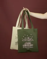 Tote bag de color beige con estampado gráfico en color verde que ilustra un perro con lentes sobre una manta, acompañado por la frase 'Otoño Uruguayo'. Cuenta con doble asa larga para llevar al hombro.