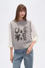 Chaleco de punto sin mangas en color beige con efecto confetti y diseño de jacquard frontal en color negro con motivos de herradura, luna y pájaro. Cuenta con cuello redondo y acabados acanalados.