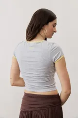 Remera corta gris melange con ribetes amarillos en el cuello y las mangas, y un estampado gráfico abstracto en el pecho.