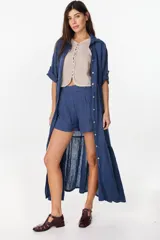Maxi vestido camisero azul de corte relajado, confeccionado en 100% lino italiano. Presenta mangas caídas con martingala, cierre frontal de botones, bajo con volado fruncido y jareta para ajustar en la cintura.