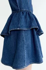 Vestido corto de denim azul con tirantes anchos, escote cuadrado, cuerpo entallado con costuras visibles y falda acampanada con doble volado en la cintura.