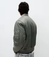 Campera tipo bomber de color verde militar, con cierre frontal, cuello, puños y cintura en tejido rib. Presenta bolsillos frontales con solapa y botón a presión, además de un bolsillo utilitario en la manga.
