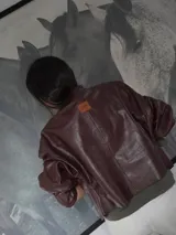 Campera de cuero con silueta oversize y corte levemente corto. Presenta cierre frontal metálico, cuello a la base y mangas amplias con detalles trenzados y recortes que aportan textura.