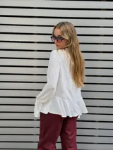 Blusa blanca de textura arrugada, con escote en V y lazos para anudar. Presenta mangas largas con puños acampanados y un diseño con volado en el ruedo.