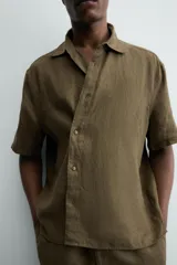 Camisa de corte relajado confeccionada en lino color verde militar, con cuello solapa, manga corta y cierre frontal de botones.